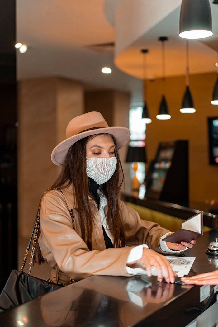 A woman wearing a mask checks into a hotel at the reception desk, highlighting safe travel.